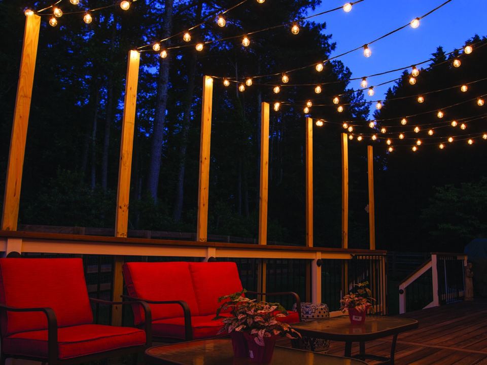 String lights over a deck with red outdoor chairs
