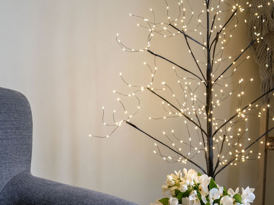 A slim fairy light tree with warm white lights beside a chair