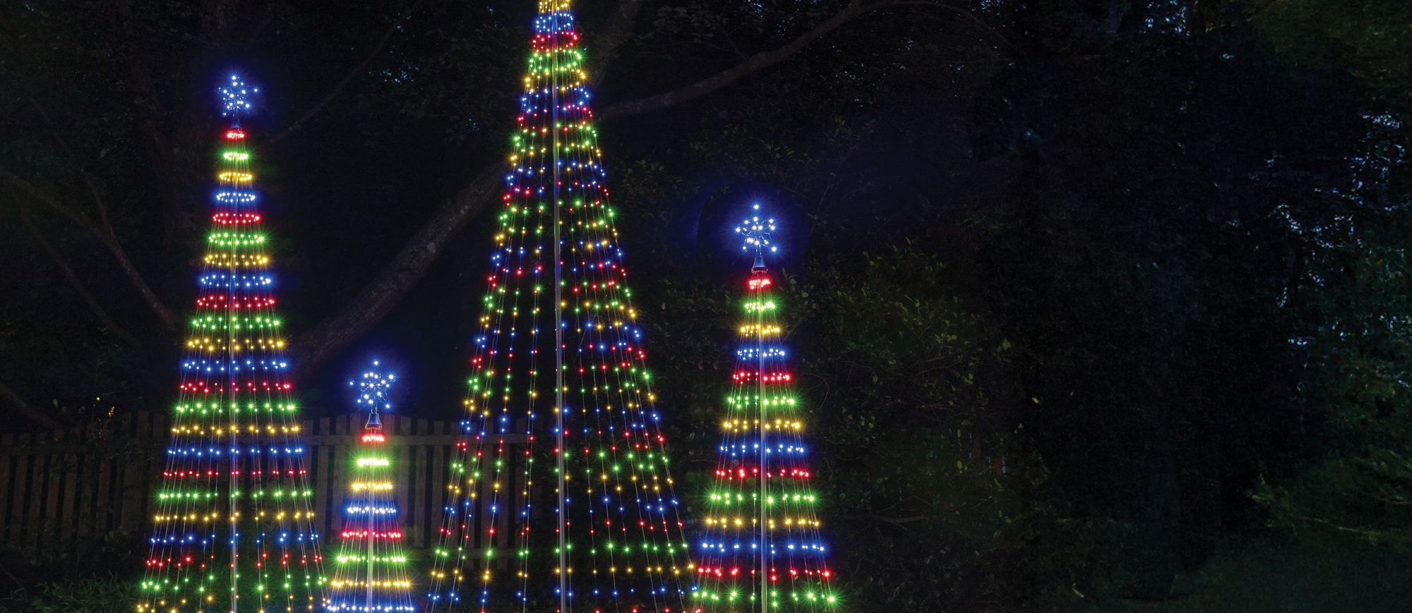Three cone-shaped light-show trees in multicolor lights on a dark lawn