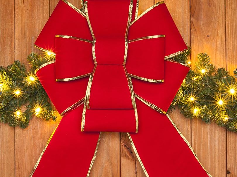 A large red bow with gold trim on a lit garland