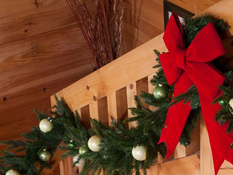 Garland with a red bow wrapped along a wooden staircase railing