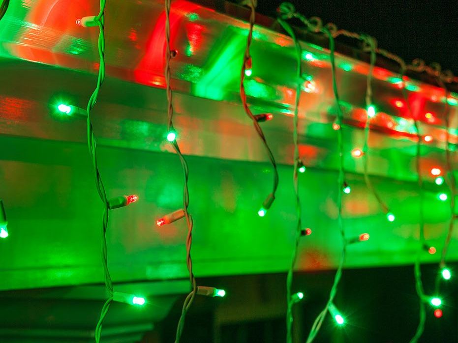 Red and green icicle lights along a porch roof