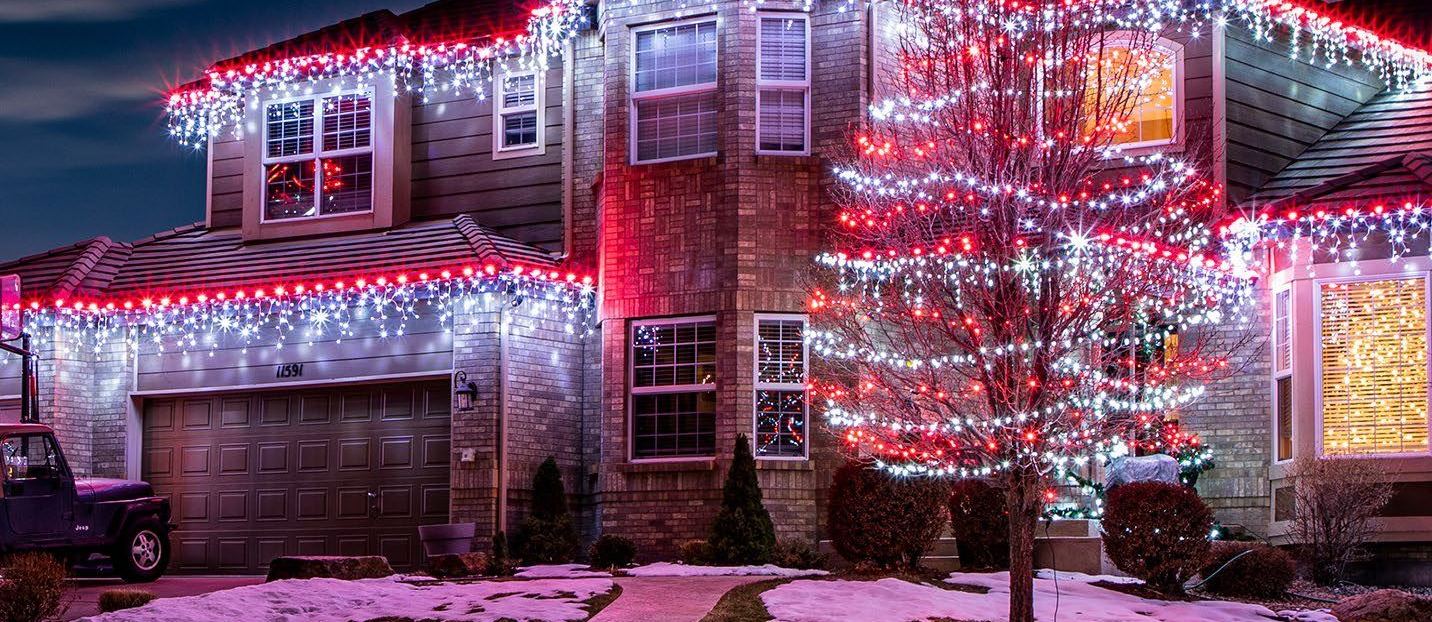 A house with icicle lights along the eaves and a tree wrapped in red and white lights