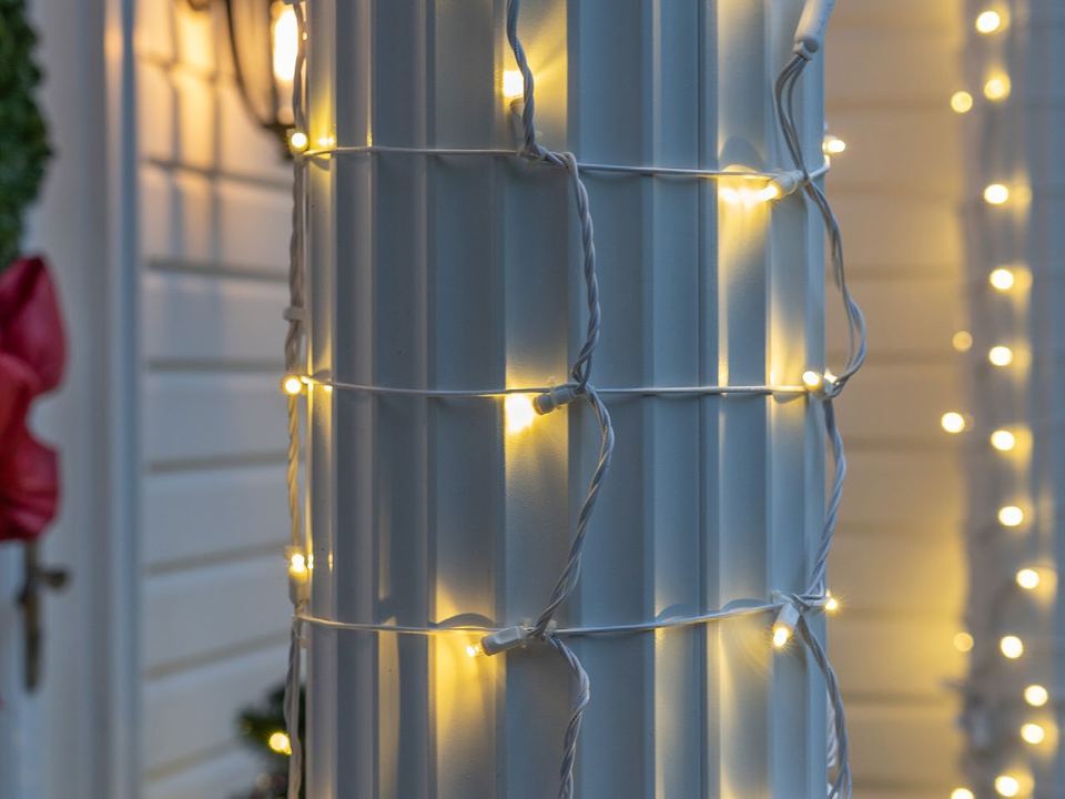 A white porch column wrapped in warm white mini lights