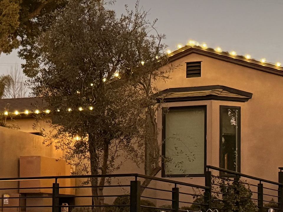 A stucco home at dusk with its rooflines outlined in warm white lights, installed by Tater Farms