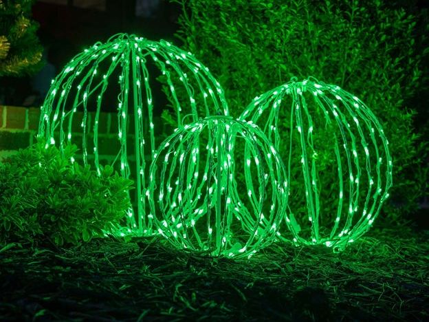 Three large green light spheres sitting in a garden bed